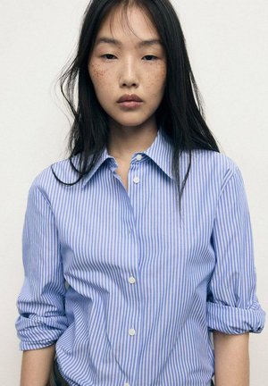 Button-up shirt featuring light blue and white vertical stripes, rolled sleeves, and a classic collar detail. Smooth cotton fabric.