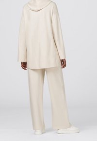 Sudadera beige de gran tamaño con capucha combinada con pantalones anchos a juego, ambos de textura suave. La modelo lleva zapatillas blancas.