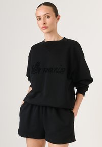 Čierna oversized mikina s textúrovaným vyšívaním "Le monie", s okrúhlym výstrihom a voľným strihom, skombinovaná s ladiacimi šortkami.