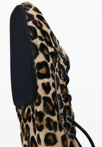 Scarpa con stampa leopardata caratterizzata da una tomaia in pelliccia testurizzata, design con lacci neri e tacco nero solido. Il colore di accento è beige con macchie marroni scure.
