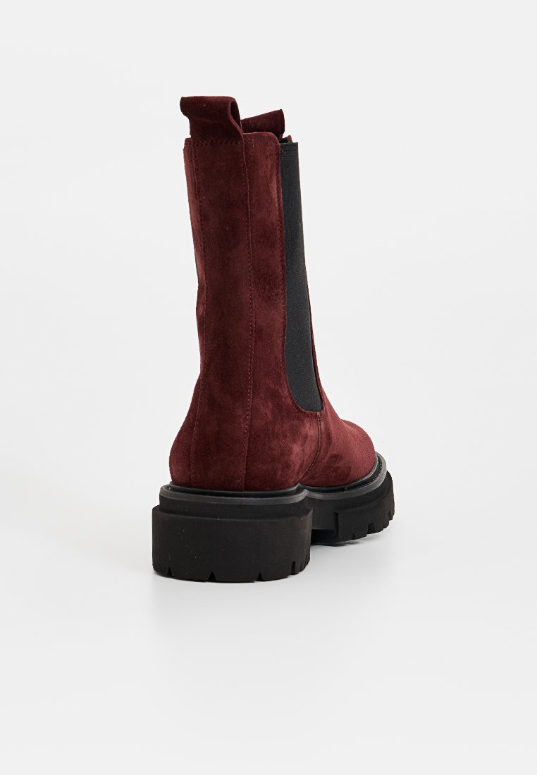 Burgunderfarbene Wildleder-Ankel-Stiefel mit einer dicken schwarzen Sohle, elastischen Seitenpaneelen und einer Zuglasche an der Rückseite für ein einfaches Anziehen.