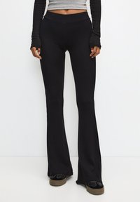 Pantalon noir évasé à côtes avec une taille haute. Le tissu a une texture douce, présentant une coupe ajustée qui s'évase à la cheville.