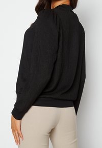 Pullover nero con texture, maniche lunghe, polsini a costine e vestibilità rilassata. Presenta dettagli arricciati sulle spalle.