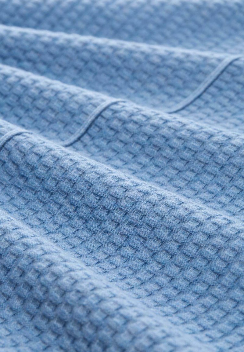 Teksturowana bawełniana tkanina w jasnoniebieskim kolorze z geometrycznym wzorem, z podniesionymi kwadratami i miękkim, tkanym wyglądem na powierzchni.