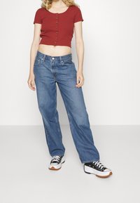 Červený pruhovaný crop top s krátkými rukávy a předními knoflíky, doplněný volnými modrými džíny a černobílými teniskami.