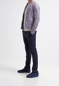 Ljust lila läderjacka med silverblixtlås, grå tröja underneath, marinblå rutiga byxor och marinblå mockasneakers.