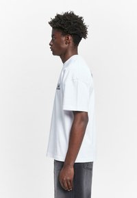 Weißes Baumwoll-T-Shirt mit kurzen Ärmeln und Rundhalsausschnitt. Das Shirt hat auf der Vorderseite gedruckten blauen Text und einen lockeren Schnitt.