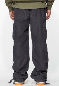 Cargo pants in dark gray, featuring multiple side pockets, a loose fit, and elastic cuffs. Made of durable fabric with visible stitching.
