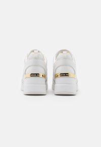 Baskets blanches avec une tige en cuir lisse, un col rembourré et des détails de talon accentués en or. Possède une semelle texturée et une plaque logo.