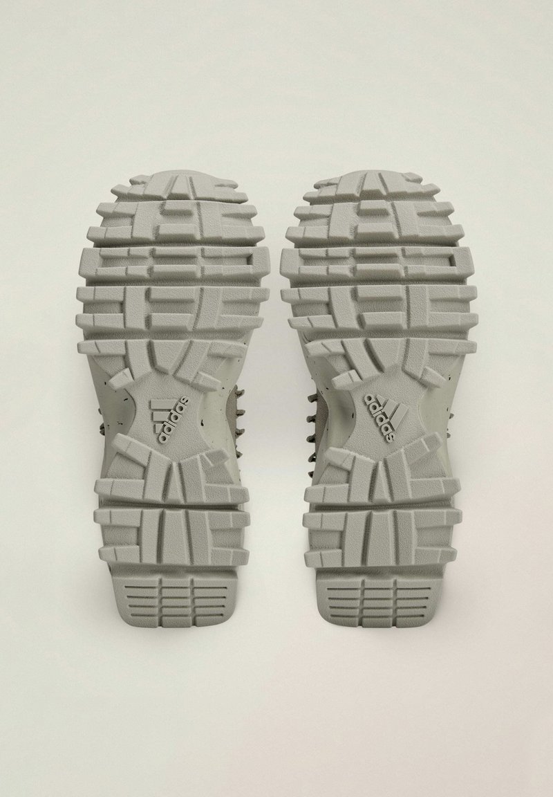 Witte sneakerzolen hebben een gestructureerd, chunky profiel met diepe groeven en een zichtbaar merklogo aan de zijkant, ontworpen voor grip.