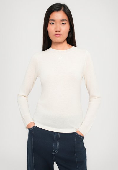 Heledad beeži pikkade varrukatega t-särk, mis on valmistatud pehmest materjalist, omab ümara kaelusega disaini ning diskreetset logo detaili rinnal. Sobitatud tummade pükstega.