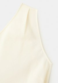 Haut sans manches couleur crème avec une large bretelle et des détails de couture subtils sur un tissu doux.