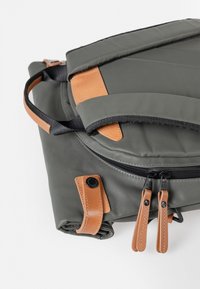 Graue Nylon-Tasche mit braunen Lederelementen, einem umschlagbaren Deckel und doppelten Reißverschlusslaschen. Strukturiertes Design mit Nähdetails.