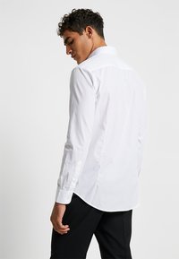 Camisa blanca de manga larga con cuello estándar, cierre de botones en la parte delantera y dobladillo recto, hecha de una suave mezcla de algodón.