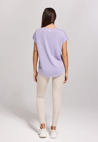 Licht lila kortärmige top met een afgeronde zoom, gecombineerd met beige leggings en witte sneakers. Eenvoudig ontwerp zonder zichtbare patronen.