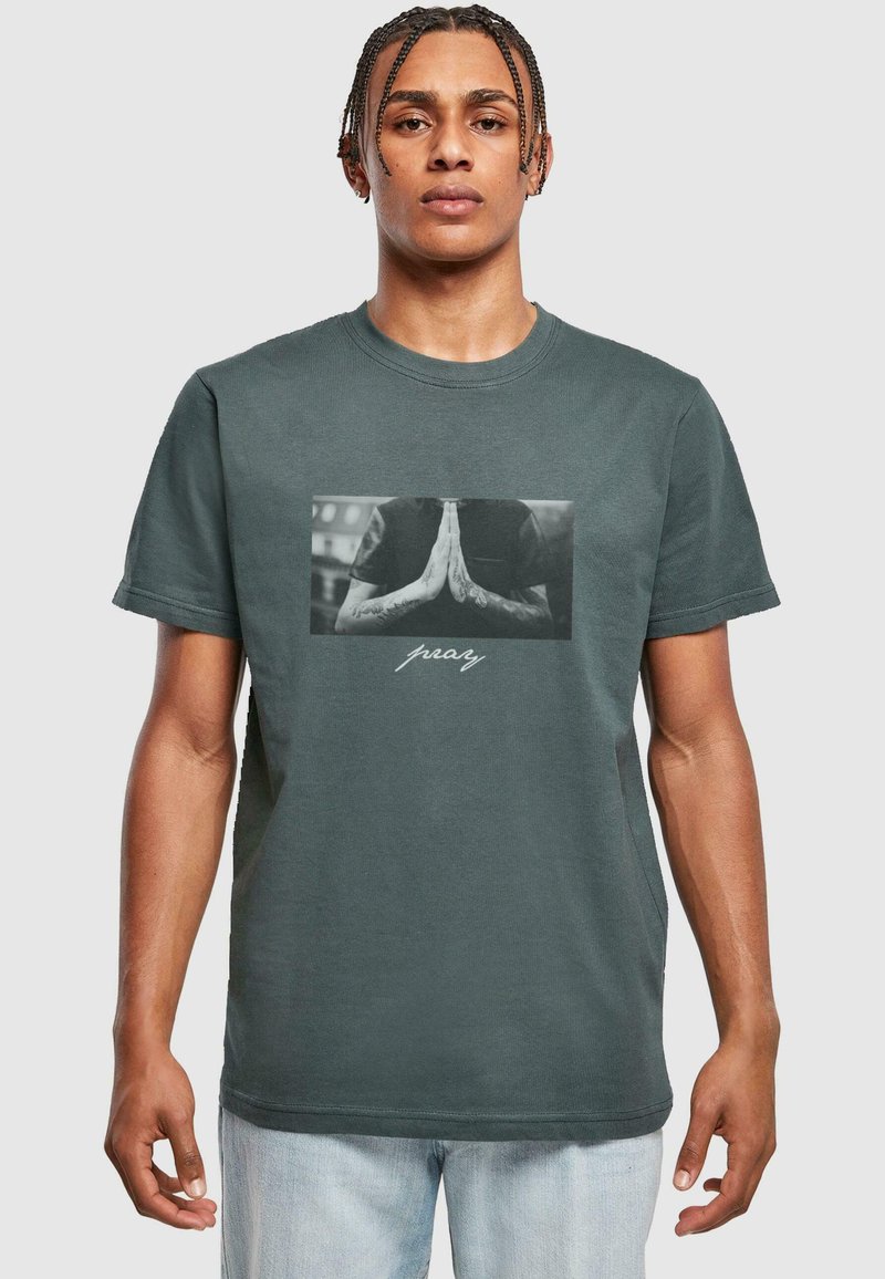 Gray cotton t-shirt featuring a front graphic of hands in a prayer position with tattoos, and the word "pray" in white script below.