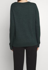Pull en maille vert foncé à coupe ample, ourlet côtelé et manches larges. Le dos présente une texture subtile sans ornements supplémentaires.