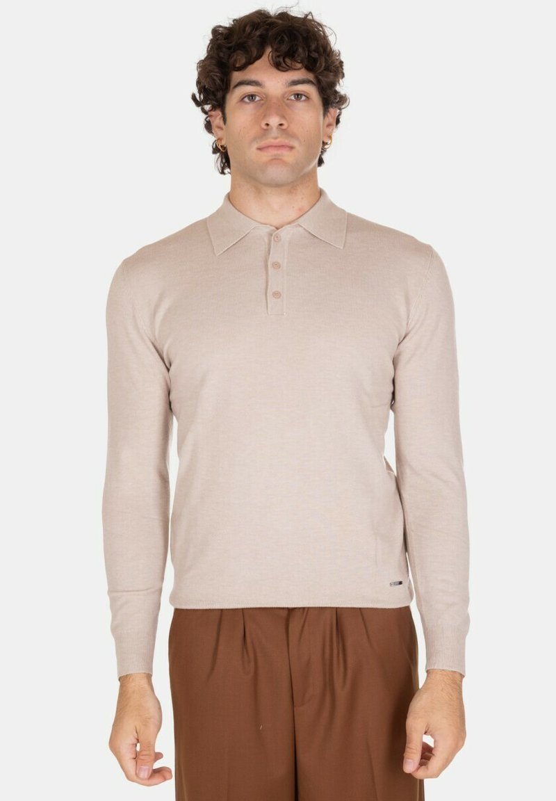 Polo a maniche lunghe beige con colletto, tre bottoni e un design aderente. Indossato con pantaloni marroni pieghettati. Texture liscia.