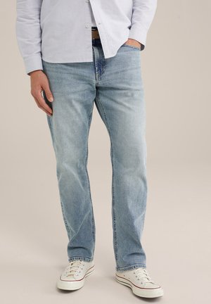 Jeans in denim blu chiaro con una vestibilità comoda, caratterizzati da un design classico a cinque tasche e bordi consumati, abbinati a sneakers in tela bianche.