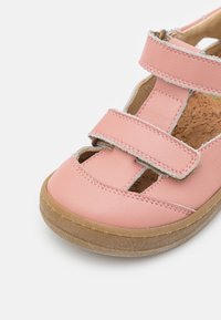 Vaaleanpunaiset nahkakengät lapsille, joissa on kaksois-Velcro-nauhat ja ruskea kumipohja, paljastaen korkkijalanpohjan sisällä.
