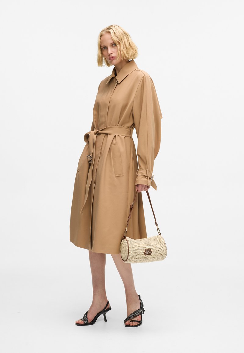 Beżowa sukienka kopertowa z kołnierzykiem, długimi rękawami, paskiem w talii oraz kieszeniami. Połączona z czarnymi sandałami na obcasie i okrągłą torebką ze słomy.