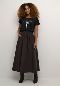 Sort t-shirt med blomstret grafik, parret med en lang, brun nederdel med elastisk talje og sidelommer. Modellen har sorte støvler på.