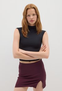 Zwarte cropped mouwloze top met een hoge hals, gecombineerd met een bordeauxrode mini-jurk met een zijsplit. Soepele stofstructuur.