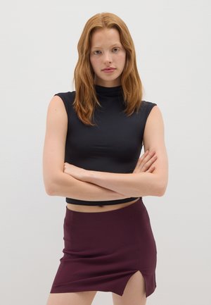 Top negro corto sin mangas con cuello alto, combinado con una falda mini burdeos con una abertura lateral. Textura de tela suave.