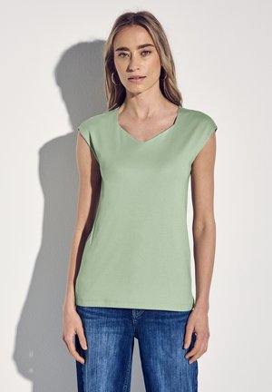Haut sans manches vert clair en V avec un tissu doux et lisse, offrant une coupe décontractée. Associé à un jean en denim bleu.