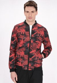 Zwarte bomberjack met een rood tropisch bladerenpatroon, rits aan de voorkant, ribgebreide manchetten en zoom. De stof lijkt lichtgewicht met een gladde textuur.