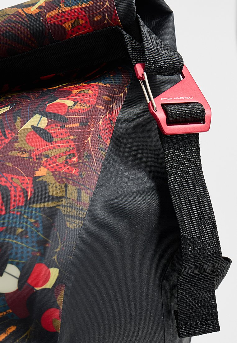 Borsa nera ecolorata con motivo, dotata di tracolla nera regolabile e fibbia metallica rossa con etichetta "Piquadro" su uno sfondo semplice.