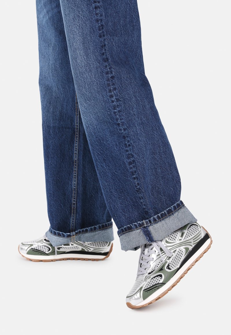 Baskets de sport argentées avec des accents verts, dessus en maille et semelles en caoutchouc, accompagnées de jeans en denim bleu retroussés.