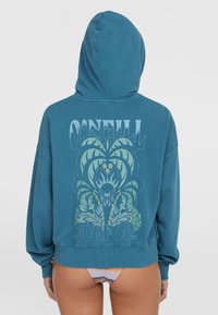 Sweat à capuche en teal. Présente un grand motif graphique bleu et vert au dos, avec des poignets et un ourlet côtelés.