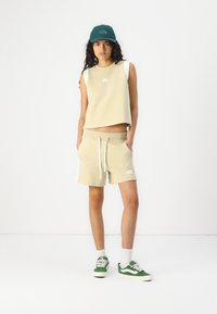 Beige ärmlös topp med vita detaljer, matchande beige shorts med dragsko och grön keps. Gröna och vita sneakers fulländar stilen.