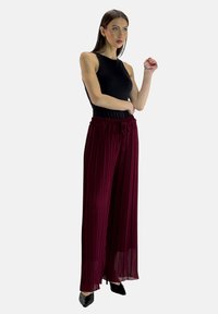 Top nero senza maniche, abbinato a pantaloni larghi plissettati color bordeaux. I pantaloni presentano una vita elasticizzata e un laccetto. Scarpe nere con punta.