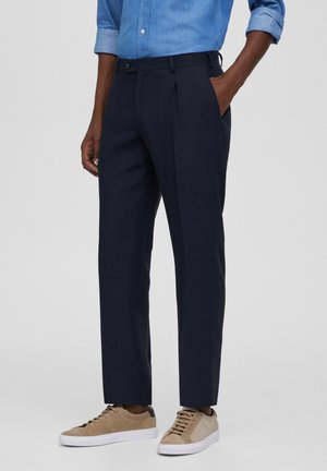 Marineblauwe broek met rechte pasvorm, gemaakt van gestructureerde stof, met voorplooien en zijzakken, gecombineerd met lichtbeige sneakers.
