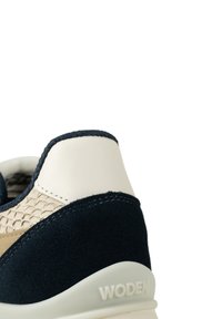Marinmocka sneakers med beige vävda läderdetaljer, krämfärgad häl och gummisula. "WODEN"-logotypen präglad på hälen.