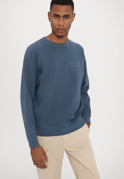 Polar din bumbac albastru, cu guler circular răsucit și mâneci lungi tip raglan. Prezintă un text brodat "DOZA ZILNICĂ DE DENIM" pe piept.