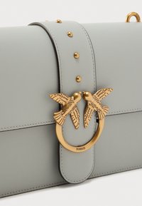 Τσάντα χειρός από ανοιχτό γκρι δέρμα με επίπεδο σχέδιο, μεταλλικά στοιχεία σε χρυσό τόνο, με δύο διακοσμητικά πουλιά σε κυκλικό κούμπωμα και διακοσμητικά καρφιά.