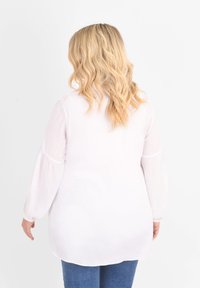 Biała bluzka z długim rękawem o luźnym kroju, z marszczeniami przy rękawach, w zestawie z niebieskimi dżinsami. Lekki, teksturowany materiał.