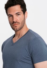 Tmavě modré tričko s výstřihem do V, vyrobené z měkké látky; má krátké rukávy a přiléhavý střih, který zvýrazňuje siluetu trupu.