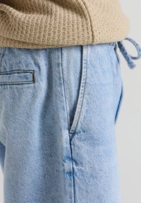 Hellblaue Denim-Jeans mit einer lockeren Passform, ausgestattet mit einer Vordertasche, sanften Verblassungen und einem Kordelzugbund zur Anpassung.