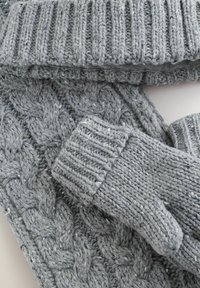 Grå stickad halsduk och vantar set med ribbat mönster och flätstickad textur, som visar upp ett mjukt, varmt och tjockt garn.