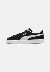 Baskets en suede noires avec une bande latérale grise, une semelle en caoutchouc blanche et des lacets noirs. Présente un logo doré et des accents blancs contrastants sur le talon.