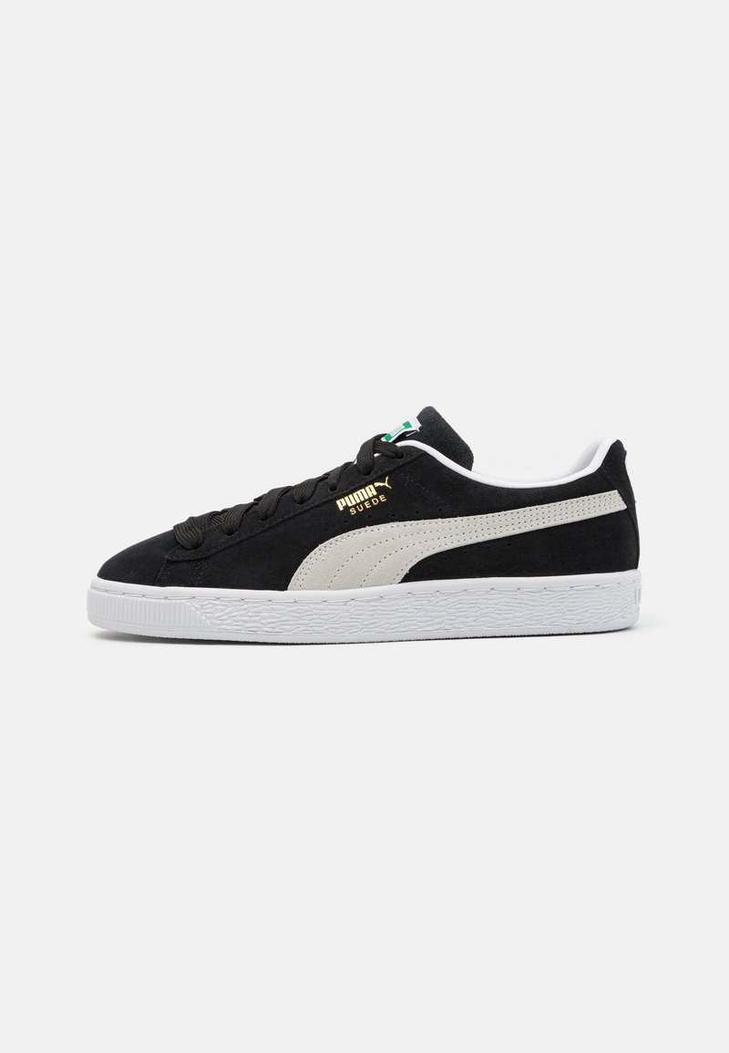 Baskets en suede noires avec une bande latérale grise, une semelle en caoutchouc blanche et des lacets noirs. Présente un logo doré et des accents blancs contrastants sur le talon.