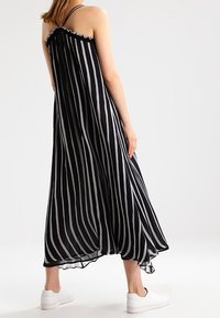 Robe maxi rayée noir et blanc avec de fines bretelles, un col volanté et une coupe fluide. Assortie à des baskets blanches.