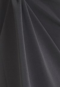 Mörkgrått tyg med en slät struktur, med subtila veck och draperingar, som illustrerar ett mjukt, deformerbart material.