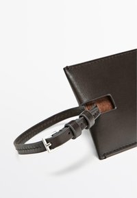 Sort læderkortholder med tekstureret finish, der har en slank rem og detalje med sølvfarvet spænde, der viser minimalistisk design.