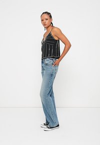 Czarny crop top w białe pionowe paski, zestawiony z jasnoniebieskimi dżinsami typu flare. Modelka nosi czarno-białe trampki.