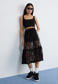 Sort blonde midi nederdel med gennemsigtige paneler, flæsekanter og sidelænger. Kombineret med en sort crop top og sorte sneakers.